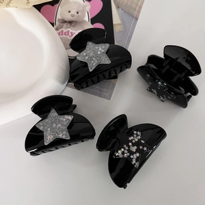 Close-up of four black Y2K star hair claws with glitter accents on a white surface