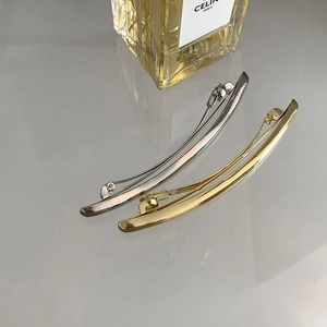 Detail view of minimalist gold and silver metal spring hair clips on a reflective surface