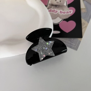 Detailed close-up of a glossy black Y2K hair claw clip with a silver glittery star accent