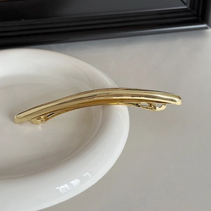 Close-up of a minimalist gold metal spring hair clip on a white ceramic plate edge