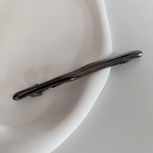 Detail of gunmetal spring hair clip with organic branch texture on a white plate