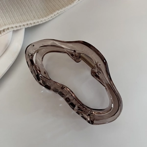 Détail d'une pince à cheveux ondulée marron translucide sur un fond en maille douce