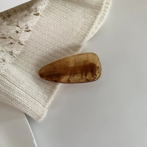 Detail of handmade amber acetate hair clip with brand lettering on a knit fabric surface