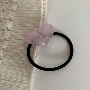 Close-up of a pink heart-shaped hair tie with marble texture on white knit background