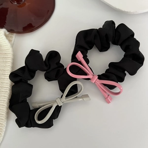 Dettaglio di elastici in raso con fiocchi di metallo opaco rosa e grigio su sfondo bianco