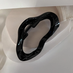 Gros plan sur la pince à cheveux noire brillante aux lignes fluides et ressort métal