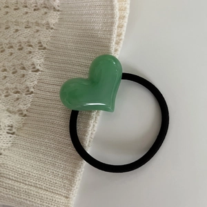 Close-up of a high-elastic black hair tie with a glossy light green resin heart bead