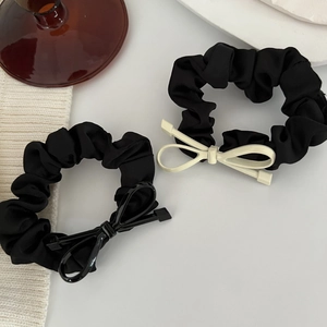 Dettaglio di due elastici scrunchie in raso nero con fiocchi decorativi 3D in primo piano