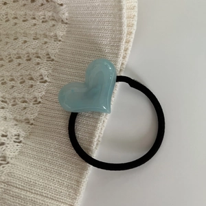 Close-up of a blue heart resin hair tie on a soft beige knit fabric background