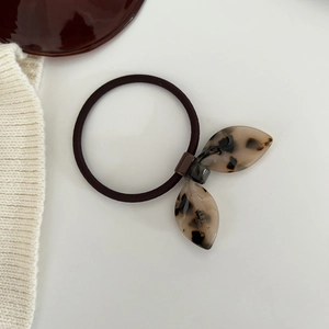 Detailed macro view of the brown elastic hair tie with tortoiseshell leaf charm and gold lettering