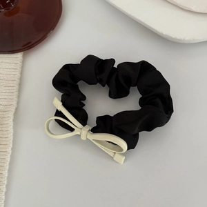 Dettaglio di un elegante elastico per capelli in raso nero con un fiocco metallico bianco