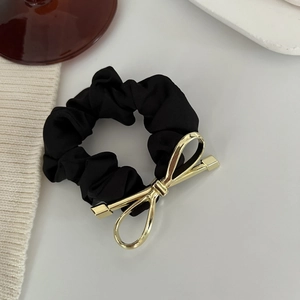 Dettaglio di un elastico per capelli in raso nero con un fiocco in metallo dorato