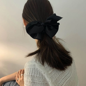 Elegant large black satin bow hair clip styled on a low ponytail for women