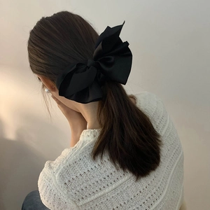 Elegant large black satin bow hair clip accessory shown on model from behind