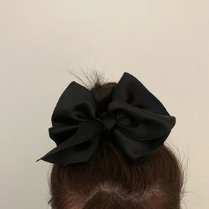 Detail view of a large black satin bow hair tie worn on a classic bun hairstyle