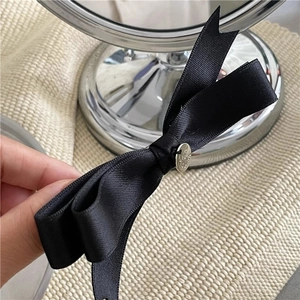 Close-up of elegant black ribbon bow hairclip with a detailed silver metal pendant