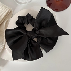 Close-up of black satin large bow hair scrunchie on a decorative white ceramic plate