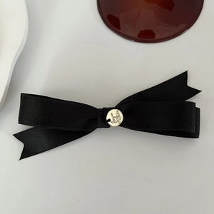 Detailed macro of black satin bow hair clip featuring a circular silver metal Juno tag