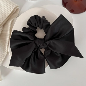 Detail of elegant black satin bow scrunchie on white plate with soft lighting