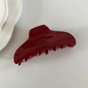 Detail showing high-gloss burgundy acetate hair claw with elegant gold lettering