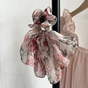 Détail du chouchou floral en mousseline rose avec un grand nœud sur un support noir