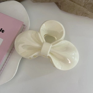 Macro detail of a cream bow hair claw clip with high-gloss glazed texture on a white tray