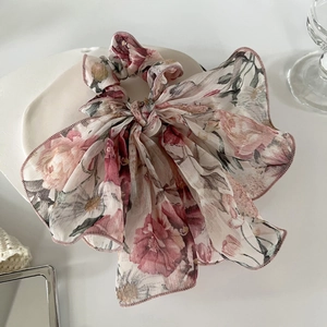 Détail d'un chouchou en mousseline florale avec longs rubans sur un plateau