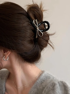 Dettaglio di elegante molletta nera con fiocco in metallo argentato indossata in uno chignon