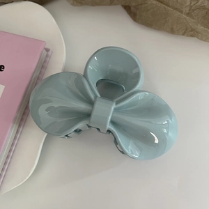 Macro shot of a light blue matte bow hair claw clip displayed on a clean white desk