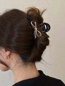 Dettaglio di una molletta per capelli nera con fiocco dorato indossata da una modella
