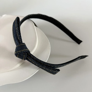 Detail of blue denim headband with bow knot and yellow contrast stitching on white ceramic