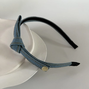 Detailed view of denim knot headband featuring yellow stitching and a golden metal buckle