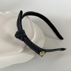 Detailed close-up of blue denim headband with gold metal tag and yellow stitching accents
