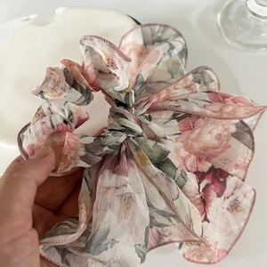 Chouchou à fleurs rose clair en mousseline avec rubans tenu dans la main