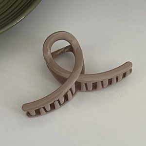Close-up of dusty pink matte hair claw clip with interlocking teeth on grey surface
