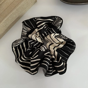 Close-up of black and white striped satin scrunchie with elegant silk-like texture and sheen