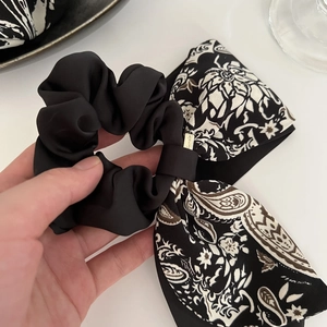 Détail d'un chouchou en satin à motif paisley avec un petit pendentif logo doré