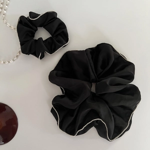 Detailed close-up of two black satin scrunchies with silver beaded edges on cream background