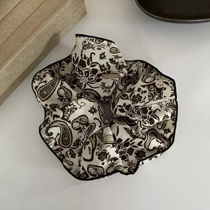 Detailed close-up of a satin paisley scrunchie with elegant black piped edges