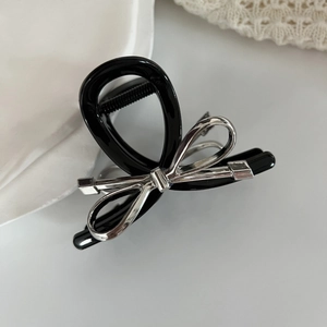 Dettaglio del fermaglio per capelli in resina nera con fiocco metallico argento su vassoio