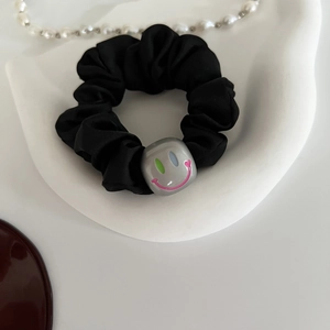 Détail d'un chouchou en satin noir avec perle smiley argentée sur un présentoir blanc