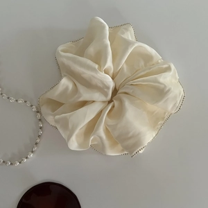 Detailed view of cream satin scrunchie with delicate faux pearl edging and soft folds