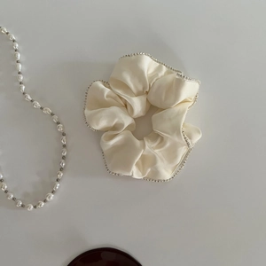 Close-up of cream satin scrunchie featuring elegant small pearl and rhinestone trim