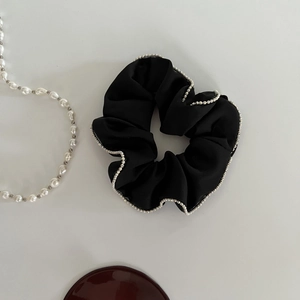 Detail of elegant black satin scrunchie with white micro pearl bead trim on smooth fabric