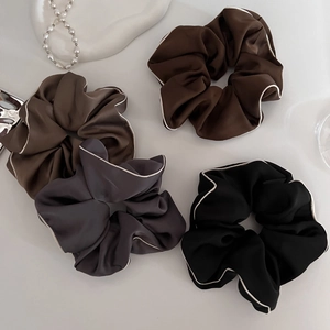 Detail of four satin scrunchies in dark tones with white piping on a minimal surface