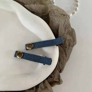 Close-up of deep blue denim hair clips with gold metal emblems on a ceramic tray