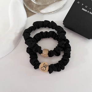 Detail of two black scrunchies featuring golden rabbit and flower metal charms
