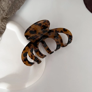 Dettaglio macro di un fermaglio per capelli tartarugato con logo oro su vassoio