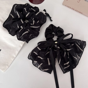 Close-up of black chiffon bow hair tie with white abstract patterns and gold buckle