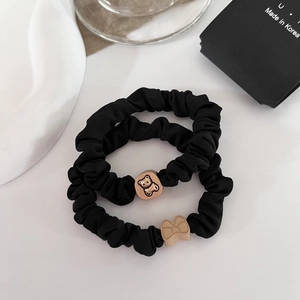 Detail of two black scrunchies with cute gold bear and bow charms on a white surface